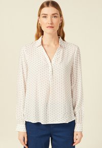 Blusa leggera in cremoso con motivo a pois blu, con chiusura a bottoni sul davanti, colletto e maniche lunghe, caratterizzata da dettagli arricciati in vita.