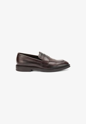 Mocassin en cuir marron avec une texture lisse, doté d'une sangle décorative et de coutures le long de la pointe. Semelle plate et design épuré.