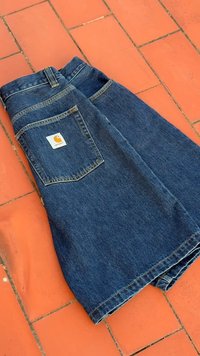 Farmer szoknya összehajtva, hátul egy logós zsebbel. Sötétkék színű, enyhe textúrával, csempézett felületen bemutatva.