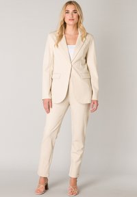 Beige op maat gemaakt pak met een gestructureerde blazer met notch revers en zakken, gecombineerd met bijpassende slim-fit broek. Gladde stofstructuur.