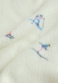 Weißer, strukturierter Stoff mit bunten, blau-, rosa- und schwarz gestickten Skifiguren, mit einer weichen, gerippten Optik.