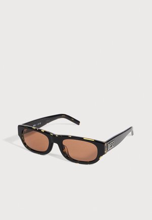 Lunettes de soleil Diesel noires, avec des verres rectangulaires bruns et des détails jaunes, présentées de biais sur un fond clair.