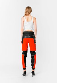 Pantalones negros y naranjas con diseño de materiales mixtos, que cuentan con bolsillos con cremallera. Combinados con una camiseta sin mangas blanca, que presenta una espalda recortada.
