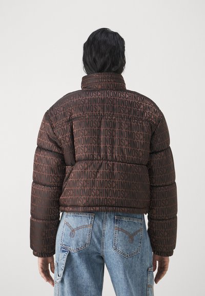 Brūns pūkains jaka ar atkārtotu tumši brūnu "MOSCHINO" logotipa rakstu, augstu apkakli un quilted tekstūru. Apvienots ar gaiši ziliem džinsiem.