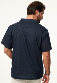 Marineblaues kurzärmliges Hemd mit einem strukturierten Blumenmuster und einer lockeren Passform. Verfügt über einen Kragen und eine Rückenpasse.