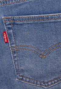 Levi's siniset farkut, joissa on keltainen ommel, punainen brändilogo ja klassinen kaareva sauma.