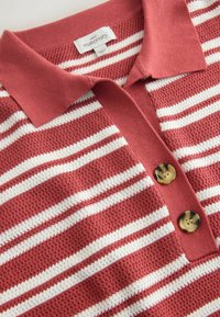 Polo de maternité à rayures rouges et blanches texturées, avec des boutons effet écaille de tortue et un col replié.