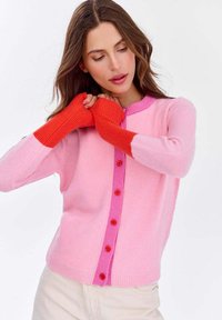 Dzianinowy kardigan w odcieniach różu i czerwieni, z kontrastującymi rękawami, okrągłym dekoltem i guzikami z przodu. Miękka tekstura i dopasowany krój.