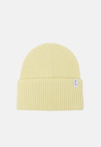 Gul ribbestrikket lue med en brettet kant, med et lite hvitt stoffmerke med svart tekst. Myk tekstur og tettsittende design.