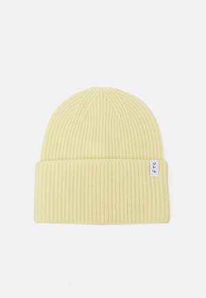 Gelbe gerippte Strickmütze mit umgeschlagenem Bündchen, ausgestattet mit einem kleinen weißen Stofflabel mit schwarzem Text. Weiche Textur und eng anliegendes Design.