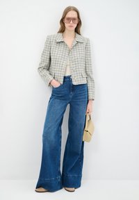 Gewatteerde, korte jas in lichtgrijs en crème; wijde blauwe jeans; beige tas; retro-stijl zonnebril; gladde textuur; op maat gemaakt ontwerp.