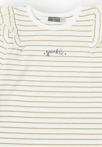 Camiseta blanca con franjas horizontales doradas, con hombros volantes y bordado azul de "brillo". Material de algodón suave, diseño casual.