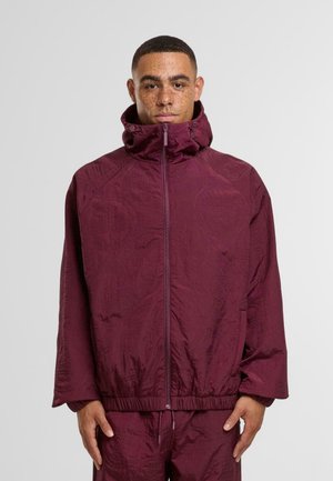 Bordeaux gesteppte Jacke mit hohem Kragen und Frontreißverschluss. Sie verfügt über elastische Bündchen und einen Saum, eine glatte Textur und dezente gestickte Muster.