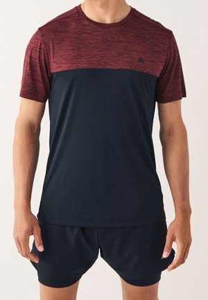 Homme portant un t-shirt de sport à manches courtes avec un haut texturé couleur bordeaux et un bas noir uni, associé à un short de sport noir.