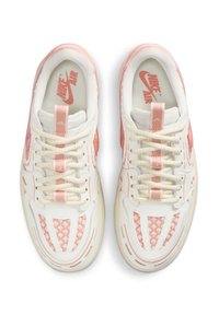 Nike Air-sneakers med vit bas, rosa detaljer, nätpaneler och diagonala designlinjer. Har beige snören och branding på sulorna.