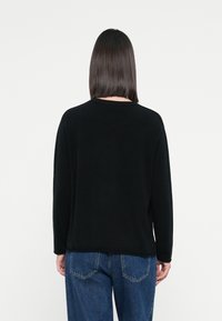 Czarny sweter z długimi rękawami, okrągłym dekoltem i luźnym krojem, w zestawieniu z niebieskimi dżinsami z tylnymi kieszeniami. Prosty i bezszwowy design.