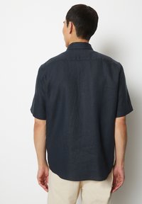 Korte mouwen, donkerblauw shirt van lichte stof, met een achterpat en een gebogen zoom, met een subtiele textuurafwerking.