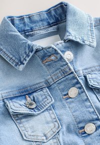 Veste en jean bleu clair avec col, boutons en métal et deux poches à rabat à l'avant avec fermetures à bouton.