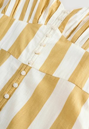 Gul og hvid stribet stof med knaplukning foran, runde knapper, samlet detaljer og en glat tekstur.
