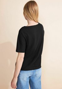 Černý krátký rukáv top s texturovaným, žebrovaným vzorem, s kulatým výstřihem a volným střihem, v kombinaci se světle modrými džíny.