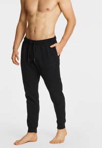 Czarne dresowe spodnie bawełniane z elastycznym pasem, regulowanym sznurkiem, bocznymi kieszeniami i ściągaczami przy kostkach. Bez widocznych logo lub wzorów.