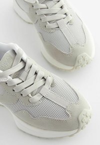 Jasnoszare sneakersy z siateczkowych i zamszowych materiałów, o zaokrąglonym kształcie, płaskich sznurowadłach i teksturowanej gumowej podeszwie z bieżnikiem.