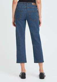 Jeans de denim azul con corte recto, cintura de altura media y dos bolsillos traseros, con dobladillo deshilachado y una textura sutil.