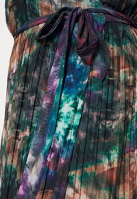 Robe plissée multicolore avec une taille ceinturée. Le tissu présente un mélange de motifs tie-dye dans des teintes de vert foncé, bleu et bordeaux.