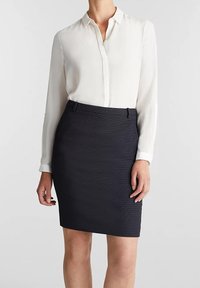 Chemise blanche à manches longues, boutonnée, rentrée dans une jupe crayon bleue marine texturée. Ajustée et arrivant au genou, avec un subtil éclat et sans motifs visibles.