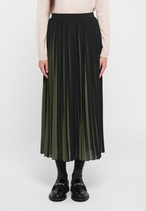 Saia midi plissada em preto e verde-oliva, com uma cintura alta, tecido fluido, e combinada com meias de tornozelo escuras e mocassins pretos.