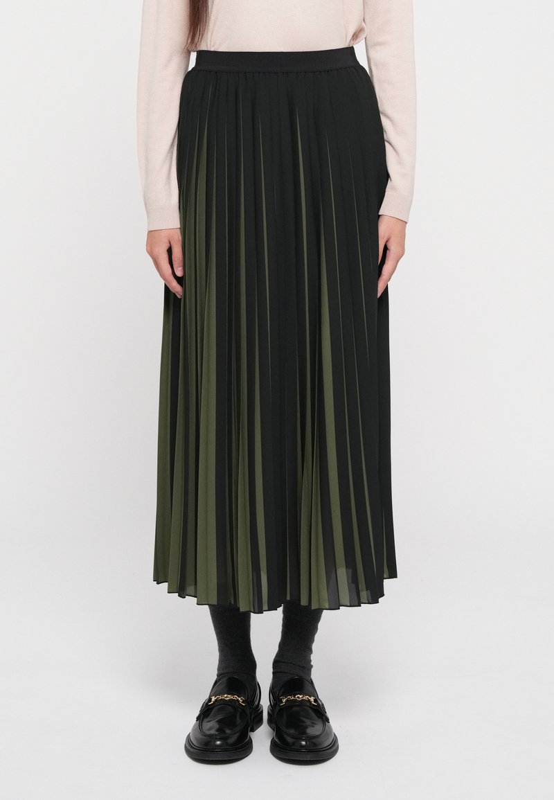 Pleated midi skirt in black and olive green, with a high waistband, flowing fabric, and paired with dark ankle socks and black loafers.