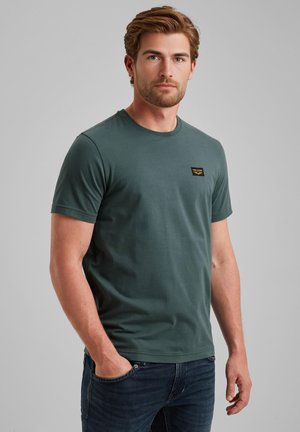Dark green cotton T-shirt with short sleeves and a crew neck. Features a small branded patch on the chest and a relaxed fit.