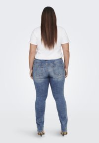 Jeans de mezclilla azul ajustados con una cintura de altura media, que presentan bolsillos traseros y un sutil efecto de desvanecimiento, combinados con una camiseta blanca.