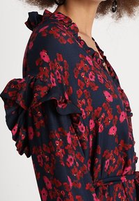 Vestido floral de fondo marino con flores rojas y rosas. Cuenta con mangas con volantes y un escote en V, fabricado en una tela suave y texturizada.