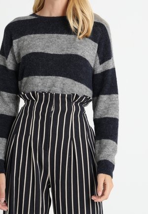 Grau und marineblau gestreifter Pullover mit Rundhalsausschnitt und langen Ärmeln, kombiniert mit hochgeschnittenen, weit geschnittenen gestreiften Hosen in Marineblau und Creme.