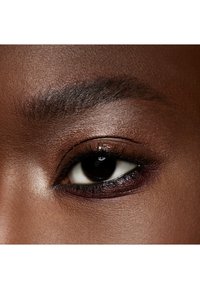 Nahaufnahme eines Auges mit einer dunkelbraunen Iris und Eyeliner, umgeben von glatter, leicht strukturierter Haut und einer gepflegten Augenbraue.
