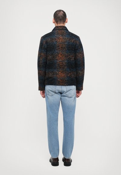 Wool-blend jacket with a dark blue and orange check pattern, featuring a classic collar and relaxed fit, worn over light blue jeans.