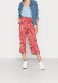 Culottes à motif floral rose avec une taille élastique, associées à un haut bleu clair et une veste en jean. Des baskets blanches complètent la tenue.