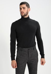 Zwarte turtleneck trui van zacht materiaal, met een getailleerd ontwerp en lange mouwen, gecombineerd met gestructureerde grijze broek.