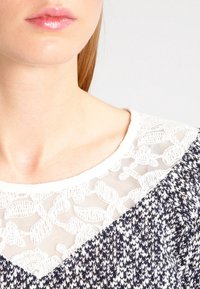 Blandning av spetskofta med en vit blommönstrad ok och en strukturerad kropp i marinblått och vitt, med en bred halsringning och avslappnad passform.