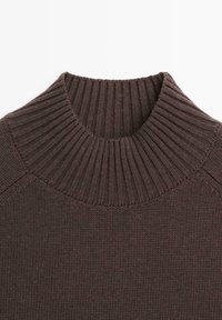 Maglione marrone scuro lavorato a maglia con un ampio colletto a dolcevita a coste e trama della maglia visibile sul corpo e sulle maniche.