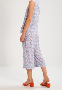 Combinaison à motifs multicolores en bleu, blanc et rouge ; design sans manches avec une coupe évasée, associée à des sandales à talons blocs orange.