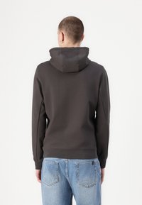 Dark gray hoodie with a structured hood, long sleeves, and ribbed cuffs. Paired with light blue denim jeans. Simple design, no visible patterns.