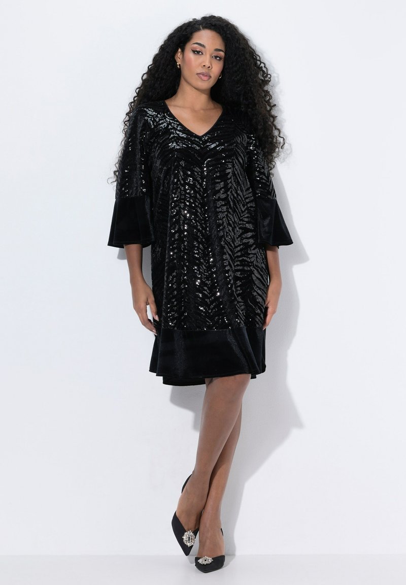 Vestido negro de lentejuelas con escote en V, mangas cortas de campana y un dobladillo negro liso; combinado con tacones negros que presentan acentos decorativos de hardware.