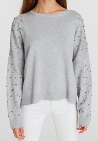 Pull-over gris clair en tissu doux, doté de manches longues ornées de clous métalliques le long des bras, avec une coupe décontractée et raccourcie.