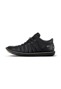 Sneaker nera in pelle con una tomaia texturizzata, lacci elastici e suola in gomma con un sottile accento verde lungo il bordo.
