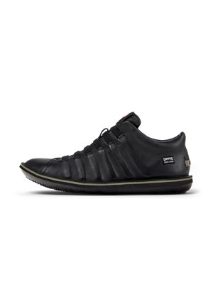 Black leather sneaker featuring a textured upper, elastic laces, and a rubber sole with subtle green accent along the edge.