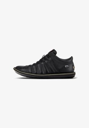 Black leather sneaker featuring a textured upper, elastic laces, and a rubber sole with subtle green accent along the edge.
