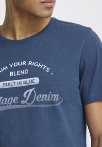 Tamsiai mėlyna medvilninė marškinėliai su apvaliu iškarpymu. Puikuojasi balta spausdinta užrašu: „Reikalaukite savo teisių - „Blend Built in Blue Vintage Denim“. 