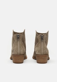 Botines de ante beige con lados perforados, tacón apilado marrón y cremallera trasera. Presenta un pequeño logo en el tacón.